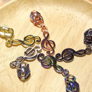 以下が含まれることがあります： トレブルクレフの形をした金属製のジッパーのプルが5つ。プルはゴールド、シルバー、ブラック、ローズゴールド、虹色です。