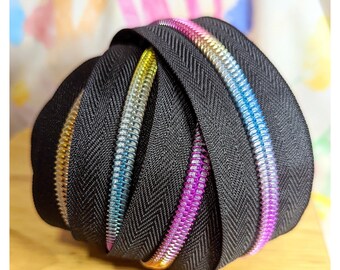 May include: A close-up of a bundle of black zipper tape with colorful zipper teeth. The zipper teeth are in shades of pink, blue, and gold.