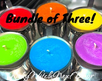 May include: A set of three candles in a bundle. The candles are in metal containers with handles. The candles are red, orange, yellow, green, blue, and purple.