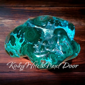 May include: A large, green and blue malachite crystal with a swirling, organic pattern. The crystal is smooth and polished, with a glossy finish.