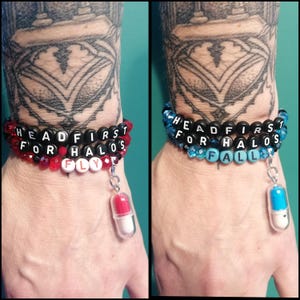 May include: Two beaded bracelets featuring black letter beads spelling HEADFIRST FOR HALOS. One bracelet has red beads and a red and white pill charm, while the other has blue beads and a blue and white pill charm with the word FLY or FALL.