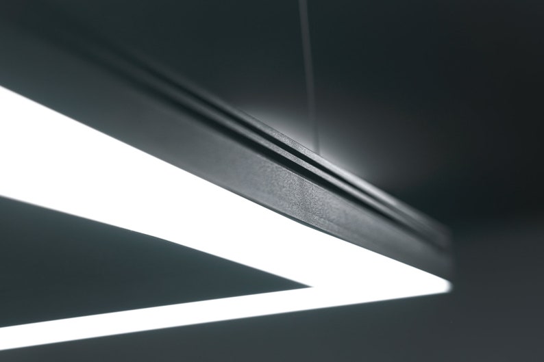 K&ouml;nnte beinhalten: Eine moderne, dreieckige Leuchte mit einem schwarzen Metallrahmen und einer wei&szlig;en LED-Lichtquelle.