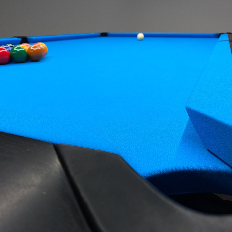 K&ouml;nnte beinhalten: Ein blauer Billardtisch mit schwarzem Filzrand und einem Satz Billardkugeln auf dem Tisch. Der Tisch hat einen schwarzen Filzrand und eine wei&szlig;e Kugel.