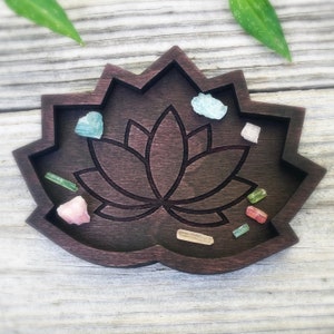 以下が含まれることがあります： 彫刻されたデザインが施された、蓮の花の形をした濃い茶色の木製トレイ。トレイには、小さなカラフルなクリスタルが敷き詰められています。