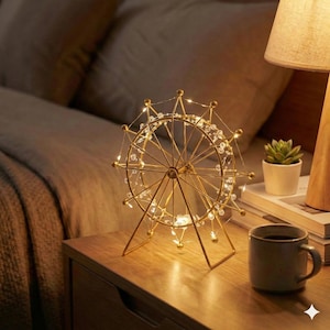 Peut inclure: Une lumière décorative dorée en forme de grande roue avec de petites lumières blanches et des accents de cristal transparent. La lumière est sur une table de chevet en bois à côté d'une tasse à café et d'une petite plante en pot.
