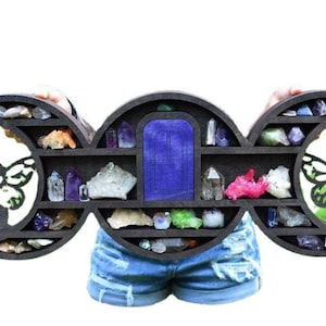 May include: A wooden triple moon shelf with a blue door in the center. The shelf is decorated with fairy silhouettes and is filled with crystals and gemstones.