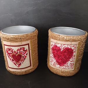May include: Two gold-colored cylindrical containers with a heart design. The hearts are made of red roses and red and pink hearts.