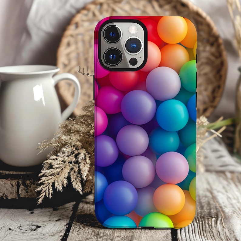 May include: A colorful phone case with a design of multi-colored balls. The case has a black camera lens cutout and a black border.