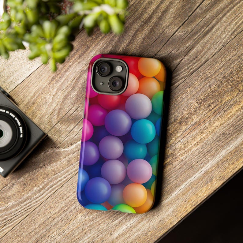 May include: A colorful phone case with a pattern of multi-colored spheres. The case has a black camera bump with two lenses.
