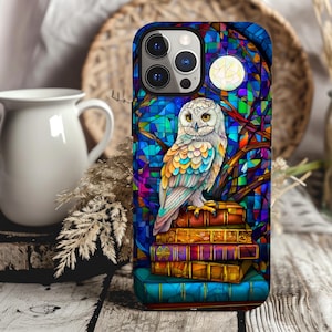 May include: A stained glass phone case featuring a white owl perched on a stack of books. The owl has colorful feathers and is surrounded by a blue, green, and purple stained glass design.