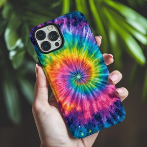 May include: A smartphone case with a vibrant tie-dye design in a spiral pattern. The case features a spectrum of colors, including pink, yellow, blue, and purple, creating a psychedelic effect. The phone case has a black camera lens border.