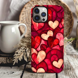May include: A red, pink, and white phone case with a pattern of hearts. The case is designed for an iPhone with a camera lens cutout.