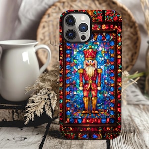 May include: A phone case with a stained glass design featuring a nutcracker in red and blue. The case has a black border and a clear camera lens.