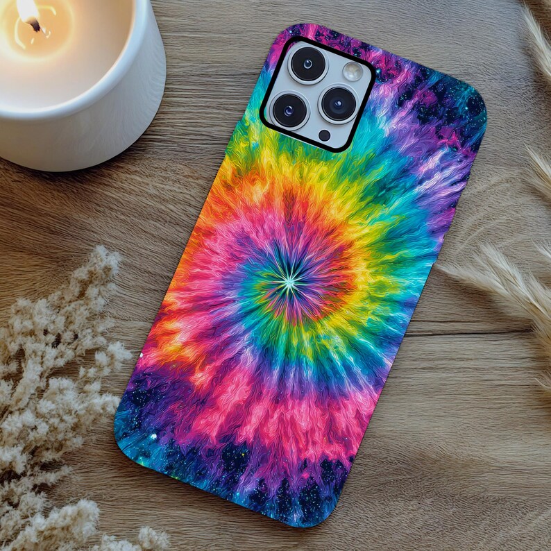 May include: A colorful phone case with a tie-dye design in a spiral pattern. The case features a vibrant mix of rainbow colors, including yellow, orange, red, pink, purple, blue, and green. The phone case is on a wooden surface.
