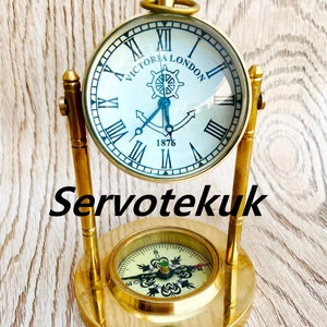 May include: A gold-toned tabletop clock with a compass base. The clock face has Roman numerals and says "Victoria London 1876".