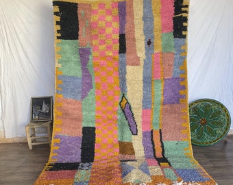 May include: A colorful Moroccan rug with geometric patterns in shades of pink, purple, blue, green, yellow, and black. The rug has a fringe border and is made of wool.