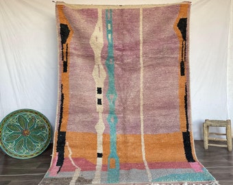 Puede incluir: Una alfombra marroquí colorida con patrones geométricos en tonos de rosa, naranja, azul y negro. La alfombra tiene un borde de flecos y está tejida con una variedad de texturas.