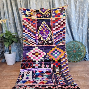 May include: A colourful Moroccan rug with a geometric pattern in shades of purple, red, yellow, and blue. The rug has a fringe border and is made of wool.