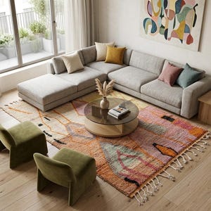 May include: A light grey sectional sofa with a chaise, two olive green low-profile chairs, and a round coffee table with a glass top. A large, multi-coloured area rug with fringe sits underneath, featuring orange, pink, and teal geometric patterns.