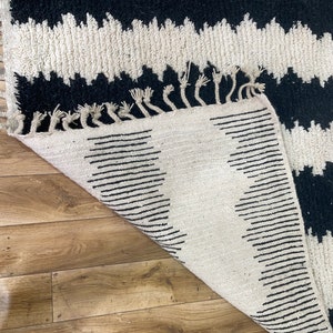 May include: A white and black rug with a zig-zag pattern. The rug has a fringe border and is folded in half.
