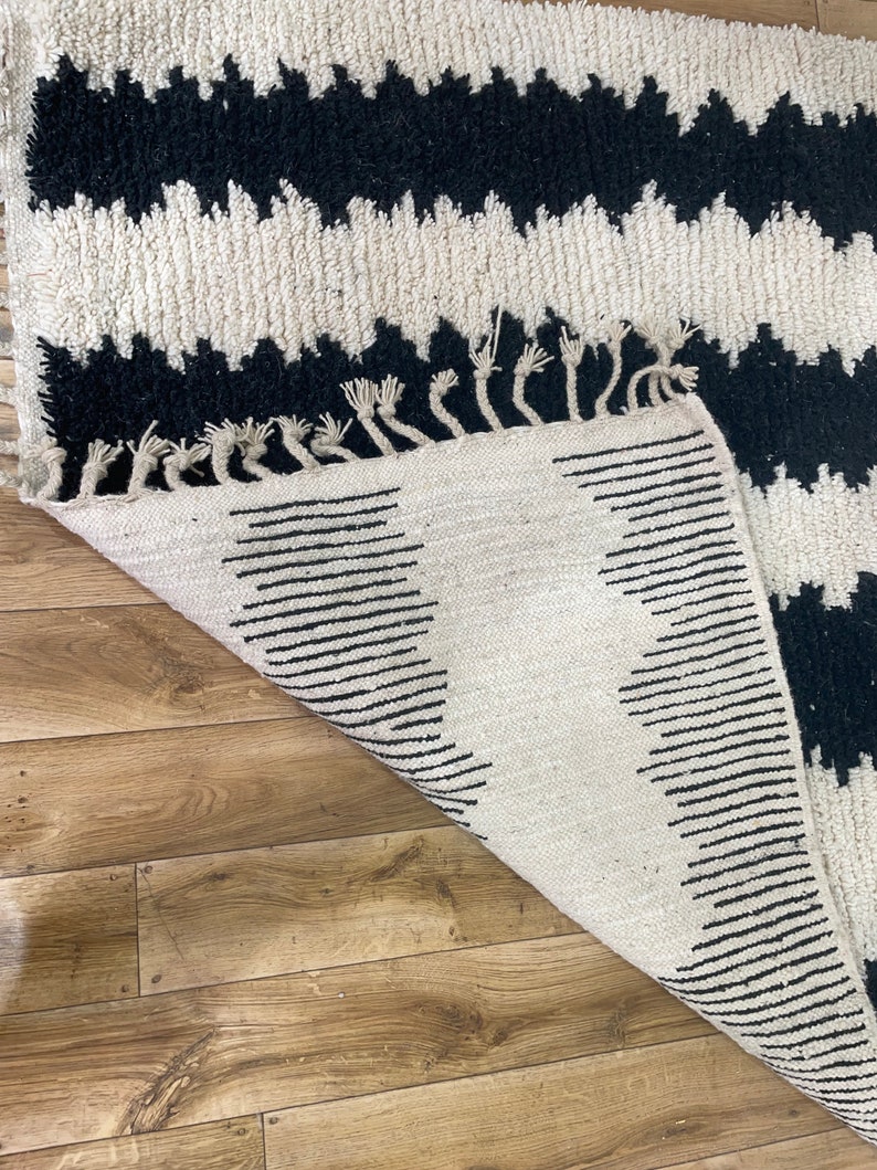 May include: A white and black rug with a zig-zag pattern. The rug has a fringe border and is folded in half.