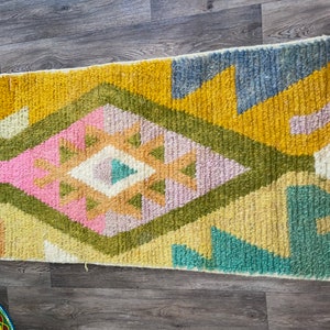 May include: A rectangular area rug featuring a high-pile texture with a central diamond motif. The design incorporates a vibrant color palette of mustard yellow, sage green, soft pink, light blue, and cream in a geometric pattern.