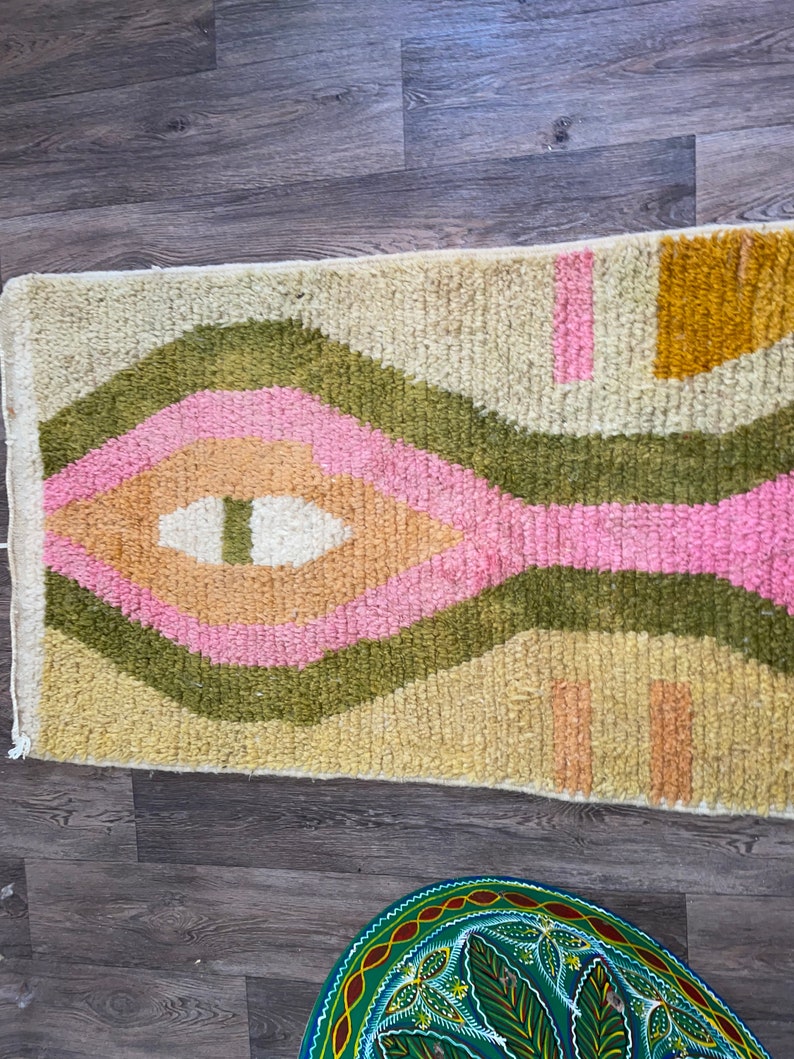 May include: A rectangular area rug featuring a high-pile texture with a cream-colored base. The design includes concentric diamond shapes in olive green, soft pink, and peach, accented by mustard yellow blocks and small pink and peach rectangular shapes.