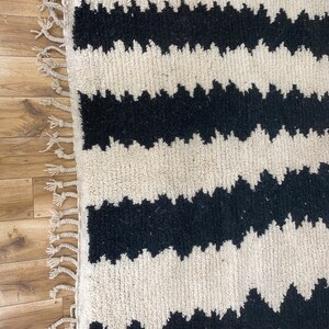 May include: Black and white rug with a wavy pattern. The rug has a fringe border.
