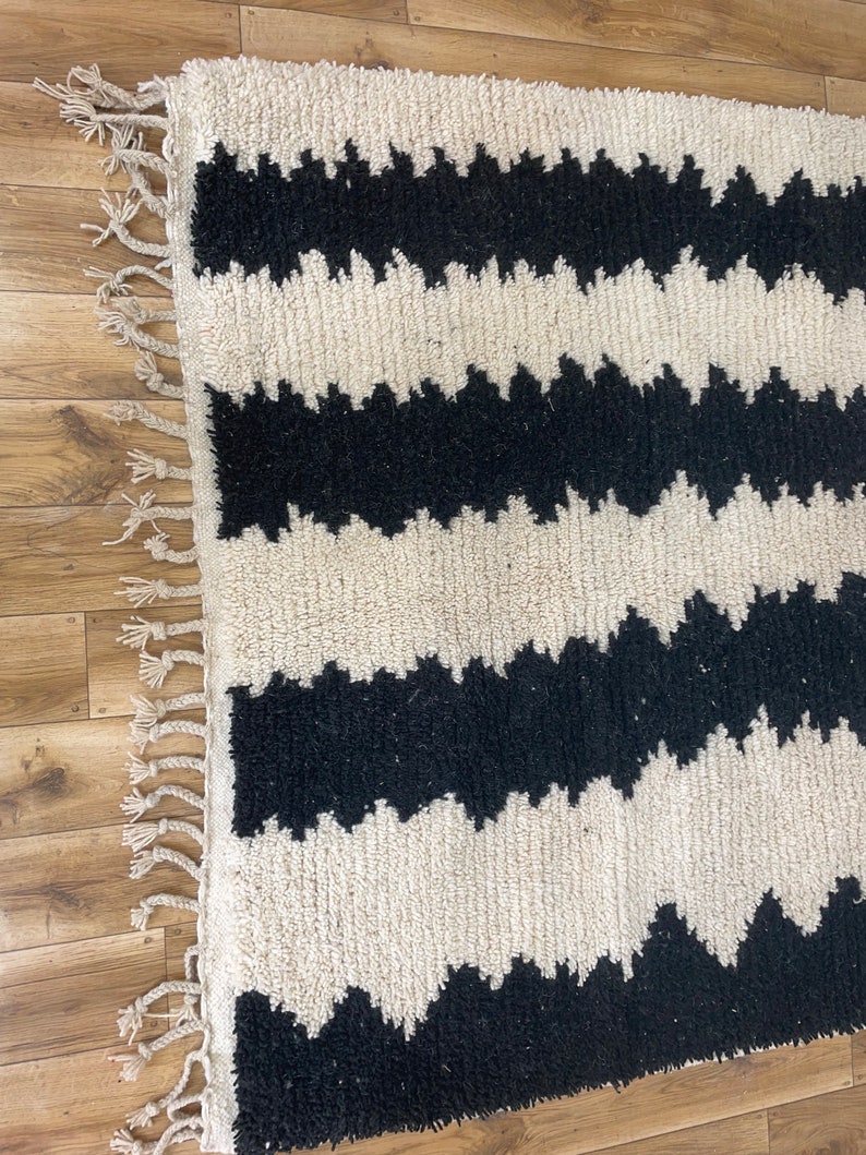 May include: Black and white rug with a wavy pattern. The rug has a fringe border.
