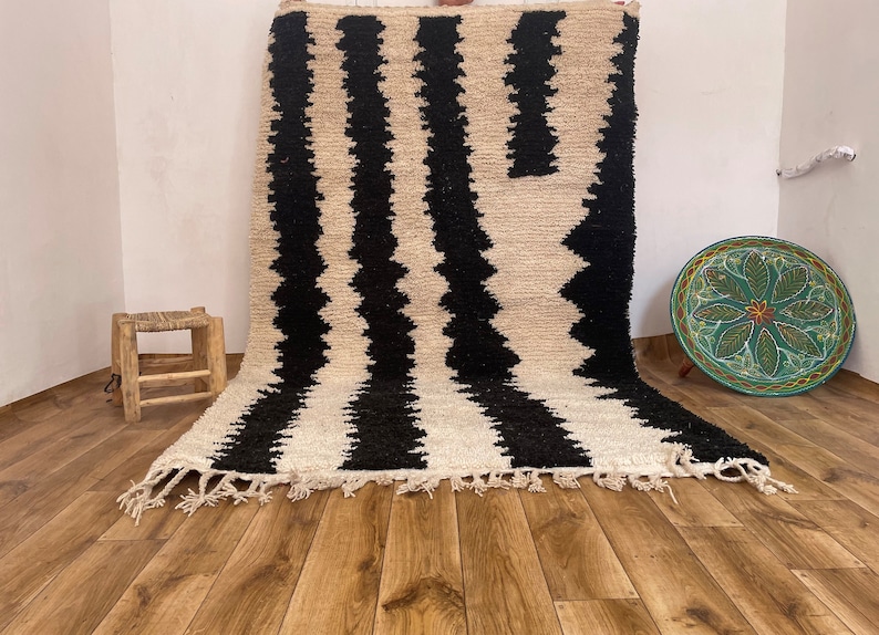 May include: Black and white striped rug with a geometric pattern. The rug has a fringe border and is made of wool.