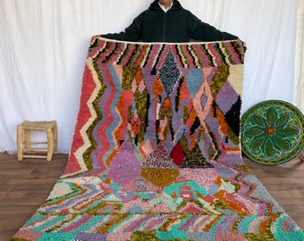 May include: A colorful Moroccan rug with geometric patterns in shades of pink, purple, green, orange, and blue. The rug has a white fringe border.