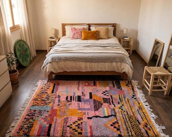 May include: A rectangular area rug featuring a vibrant, multi-coloured geometric pattern with dominant shades of pink, yellow, blue, and black. The rug has a textured, shaggy pile and is finished with white fringe detailing along the shorter edges.