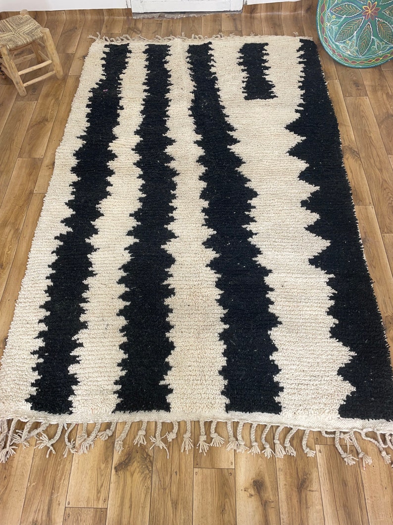 May include: Black and white striped rug with a geometric pattern. The rug has a fringe border and is made of a soft, fluffy material.