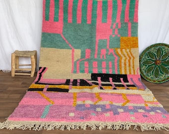 May include: A colourful Moroccan rug with geometric patterns in pink, green, yellow, black, and white. The rug has a fringe border and is woven with a variety of textures.