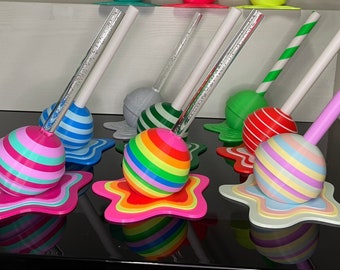 May include: A set of six colorful lollipop-shaped pen holders with striped designs and melting bases. Each holder has a different color scheme and a clear or striped straw.