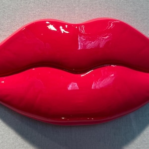 Könnte beinhalten: Ein Paar leuchtend rosa, glänzende, geformte Lippen. Die Lippen sind geschlossen und haben eine glatte, glänzende Oberfläche.