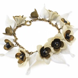 May include: A gold chain bracelet with white flower charms and black bead centers. The flowers have a delicate, layered design.