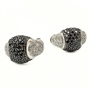 May include: A pair of luxury earrings. Each earring features a central section covered in small black stones, flanked by sections of smaller, clear stones. The earrings have a silver-colored metal setting and a rounded shape.