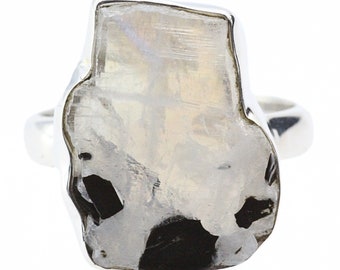 May include: A silver ring with a large, white, opaque gemstone set in a rough, irregular shape. The gemstone has black inclusions throughout.