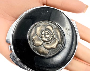 Espejo compacto coleccionable de latón con centro floral, baño de plata y esmalte negro.