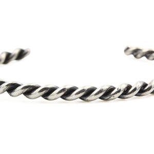 May include: A silver-toned cuff bracelet featuring a continuous twisted rope design. The metal has a darkened, oxidized finish within the grooves of the twist, creating a high-contrast appearance along the entire length of the open-ended band.