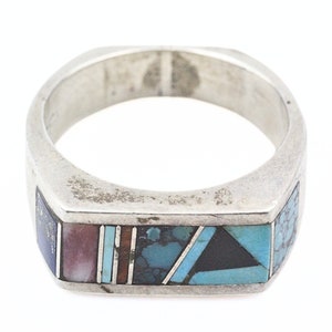 Puede incluir: Un anillo de plata con una incrustación rectangular de turquesa, lapislázuli y otras piedras.