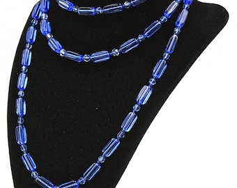 Op de afbeelding: Een blauwe glazen kralenketting op een zwarte fluwelen standaard. De ketting bestaat uit meerdere strengen kralen, waarbij elke streng rechthoekige kralen heeft.