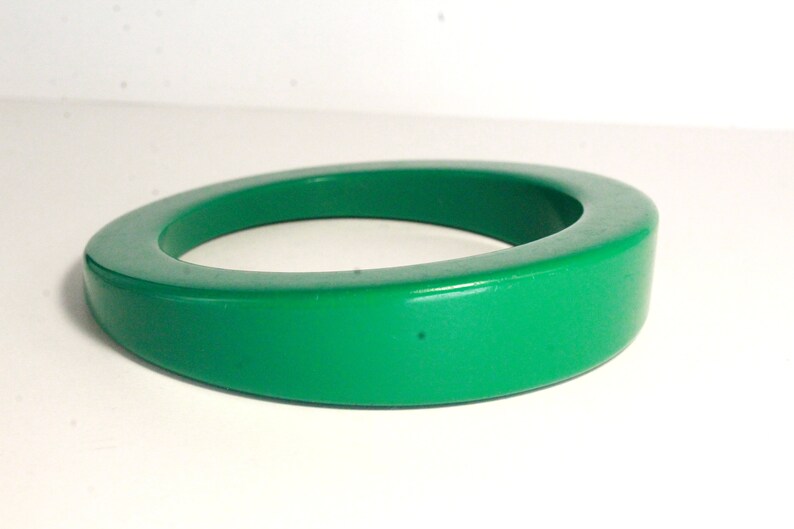 May include: A bright green plastic bangle bracelet. The bracelet is thick and has a rounded shape.