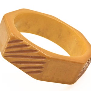 May include: A beige plastic bangle bracelet with a geometric design. The bracelet has a ridged pattern on the outside and a smooth interior.