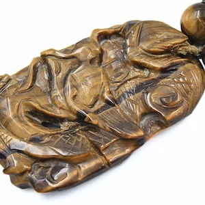 May include: A carved tiger's eye pendant necklace with a brown and gold color scheme. The pendant is intricately carved with a detailed design and is attached to a string of tiger's eye beads.