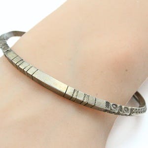 以下が含まれることがあります： 幾何学模様のシルバーカラーのバングルブレスレット。長方形と正方形のシリーズとエッチングされたディテールが特徴です。ブレスレットの直径は約6.35cmです。
