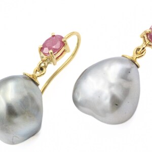 May include: A pair of gold earrings with a ruby gemstone and a large, gray pearl. The ruby is set in a gold bezel, and the pearl has a smooth, irregular shape. The earrings are displayed against a white background.