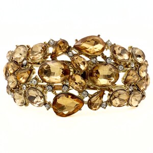 May include: A gold-toned bracelet featuring a cluster of amber-colored, faceted gemstones in various shapes and sizes. Small, clear crystals are interspersed among the larger stones. The bracelet has a hinged design.