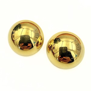 May include: A pair of polished gold-tone dome-shaped stud earrings with a smooth, reflective surface. The rounded metal surfaces show a clear mirror-like finish that captures the surrounding environment in a bright, golden hue.